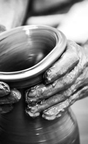 Hands of a man creating pottery on wheel, monochrome vintage view